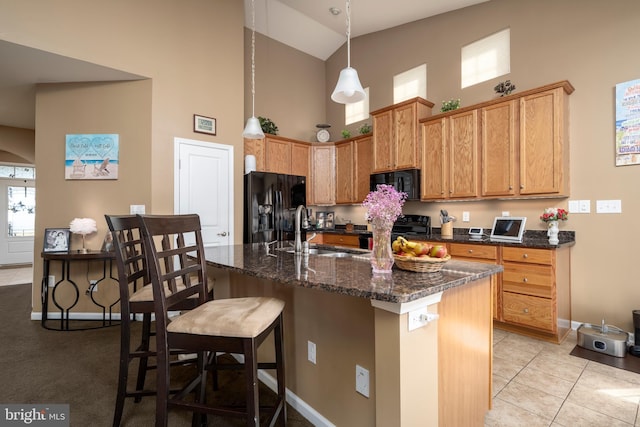 kitchen featuring sink, light tile patterned floors, a high ceiling, black appliances, and an island with sink