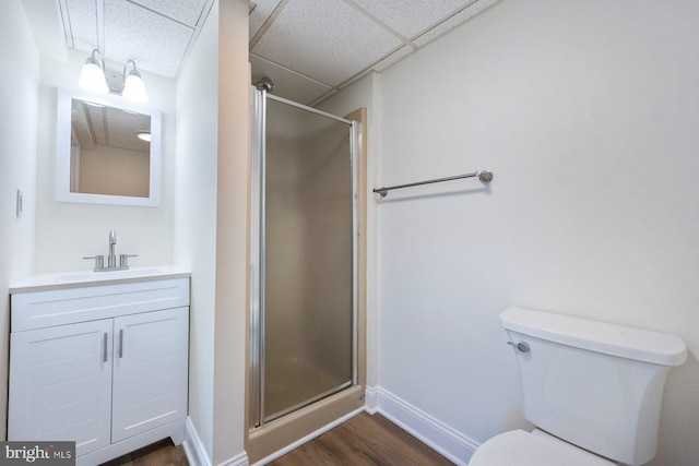 bathroom featuring toilet, a shower with shower door, a paneled ceiling, wood-type flooring, and vanity