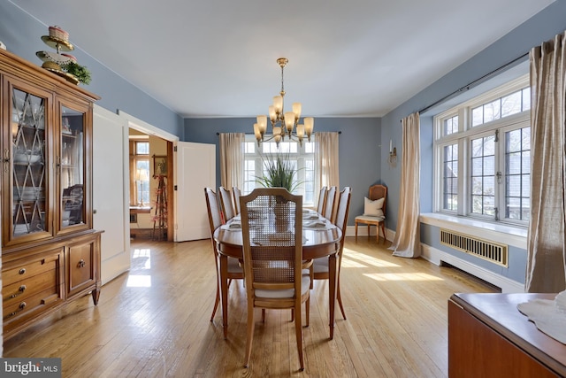 dining area with a notable chandelier, radiator heating unit, and light wood-type flooring