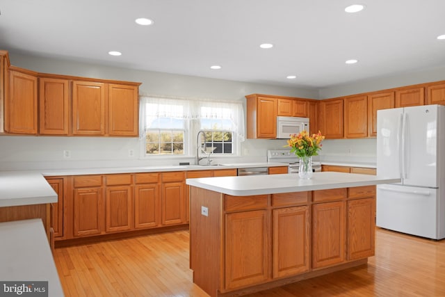 kitchen featuring white appliances, a center island, sink, and light wood-type flooring