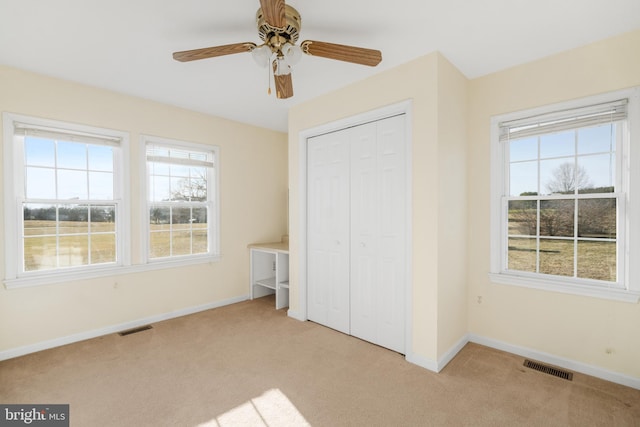 unfurnished bedroom with multiple windows, light carpet, a closet, and ceiling fan