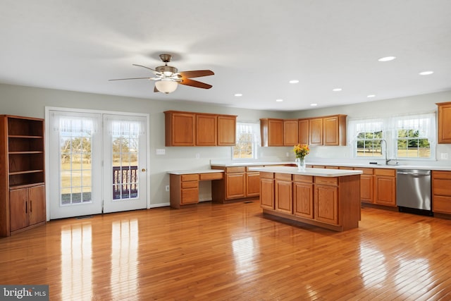 kitchen with sink, stainless steel dishwasher, a kitchen island, a wealth of natural light, and light hardwood / wood-style floors