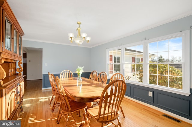 dining area featuring crown molding, light wood-type flooring, and a chandelier