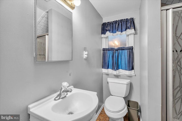 bathroom with toilet, sink, and a shower with shower door