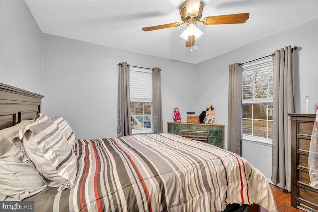 bedroom with ceiling fan, wood-type flooring, multiple windows, and an AC wall unit