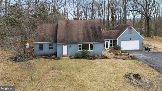 cape cod-style house with a chimney, a shingled roof, a front yard, a garage, and driveway