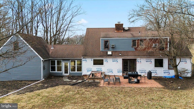 rear view of property with a patio, roof with shingles, a chimney, and a lawn