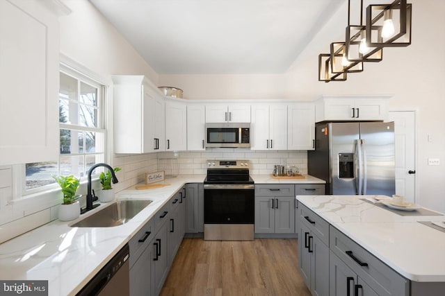 kitchen with sink, backsplash, stainless steel appliances, white cabinets, and decorative light fixtures