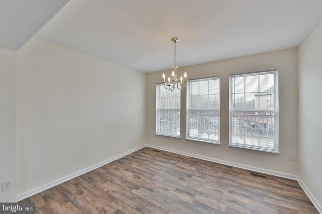 spare room with an inviting chandelier and hardwood / wood-style floors