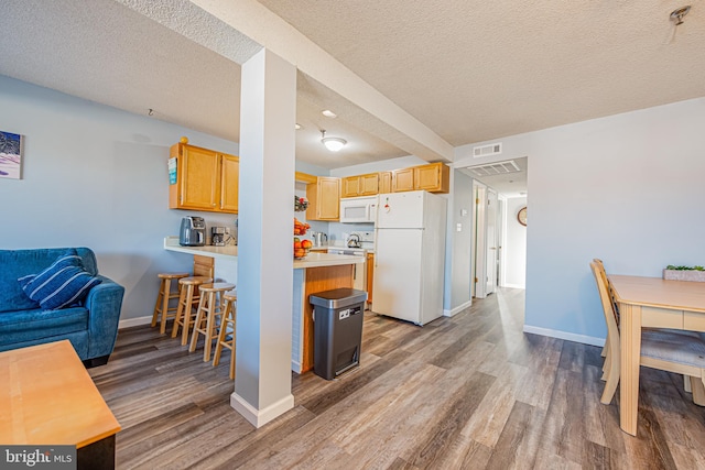 kitchen with white appliances, light brown cabinets, a textured ceiling, and hardwood / wood-style flooring