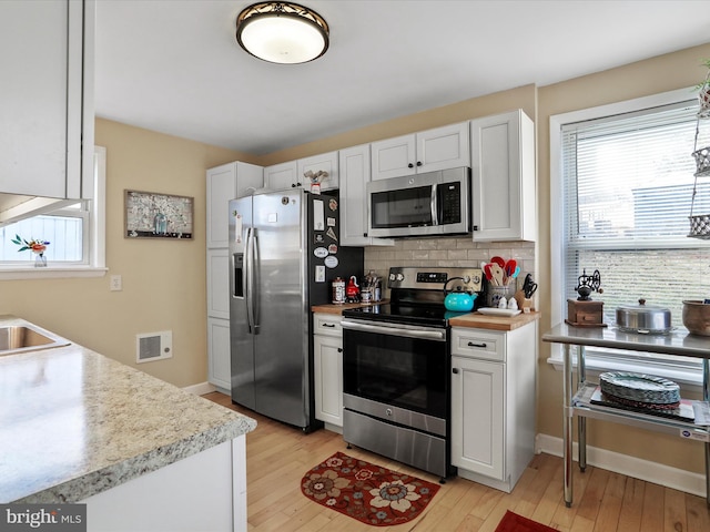 kitchen with white cabinetry, tasteful backsplash, stainless steel appliances, and light hardwood / wood-style flooring