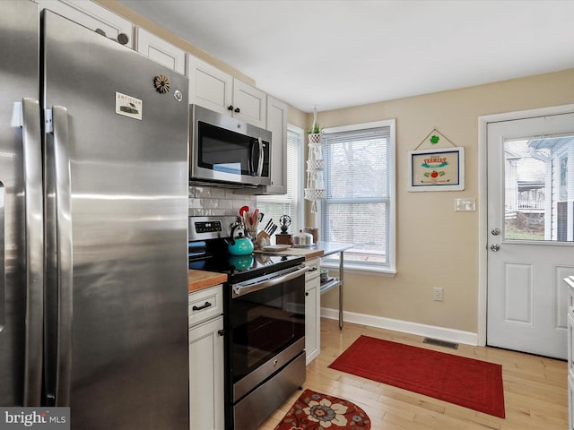 kitchen featuring white cabinetry, stainless steel appliances, light hardwood / wood-style floors, and decorative backsplash