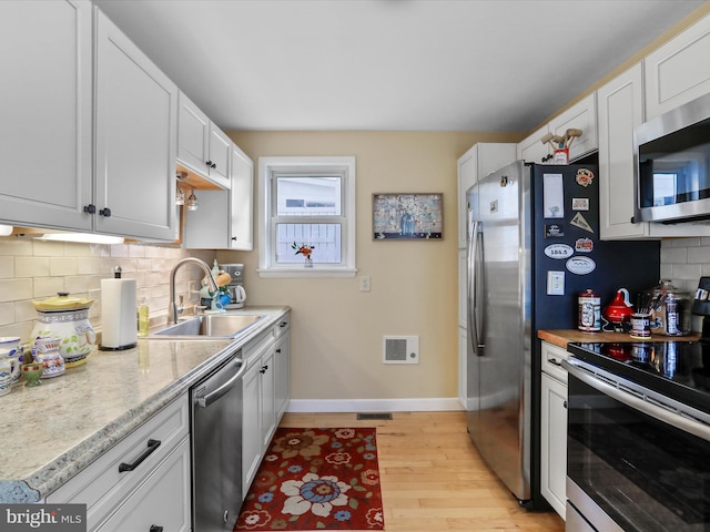 kitchen with sink, light hardwood / wood-style flooring, appliances with stainless steel finishes, white cabinetry, and backsplash