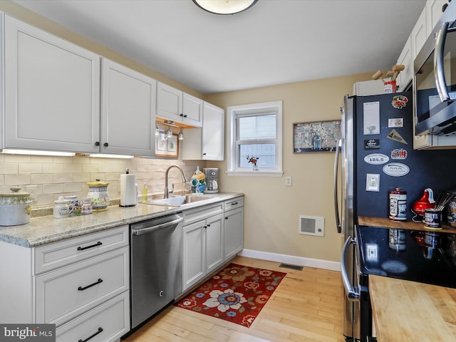 kitchen with sink, light hardwood / wood-style flooring, backsplash, stainless steel appliances, and white cabinets