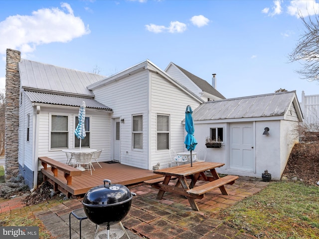 rear view of property featuring a wooden deck, an outdoor structure, and a patio