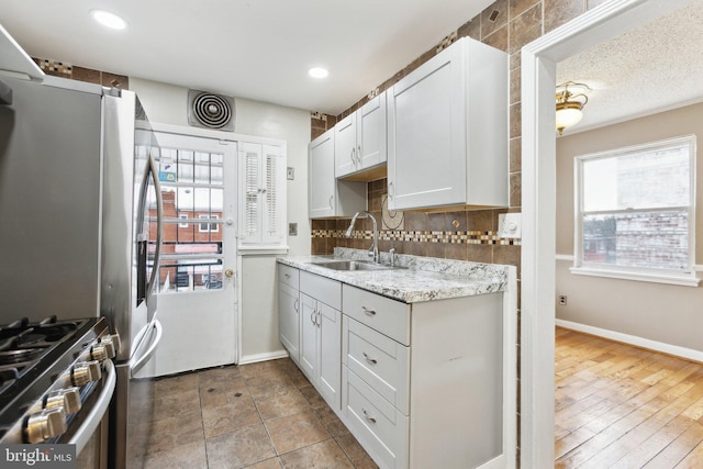 kitchen featuring white cabinetry, sink, backsplash, light stone counters, and stainless steel appliances