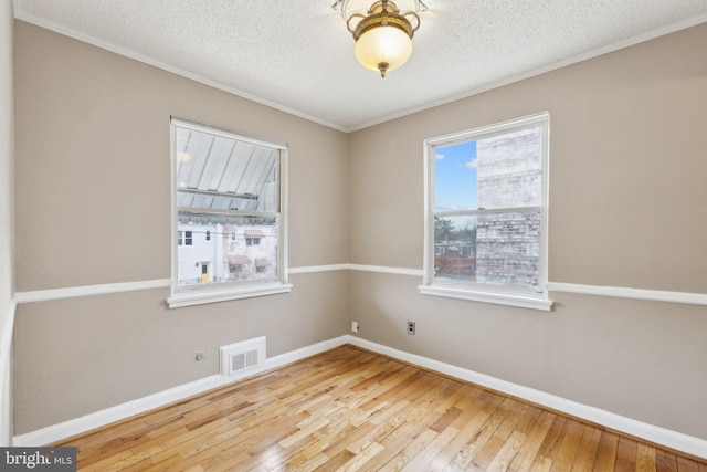 empty room with ornamental molding, light hardwood / wood-style floors, and a textured ceiling