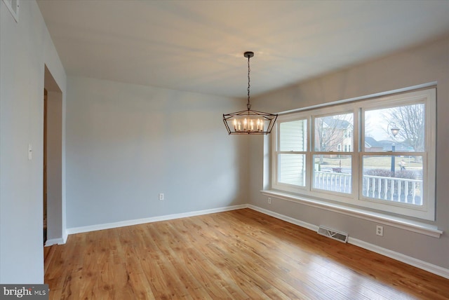 empty room with light hardwood / wood-style flooring, a notable chandelier, and plenty of natural light