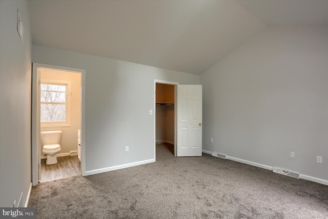 unfurnished bedroom with connected bathroom, lofted ceiling, carpet floors, a walk in closet, and a closet