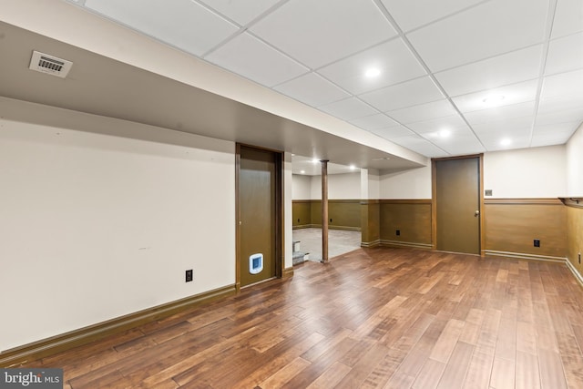 basement with a paneled ceiling, hardwood / wood-style floors, and wood walls