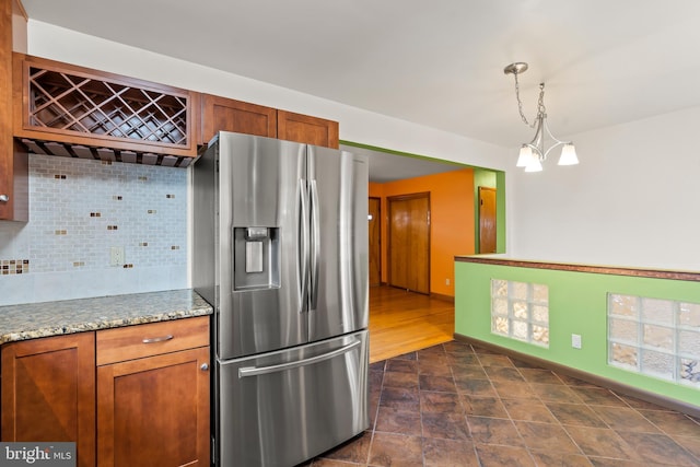 kitchen with pendant lighting, stainless steel fridge, decorative backsplash, light stone countertops, and an inviting chandelier