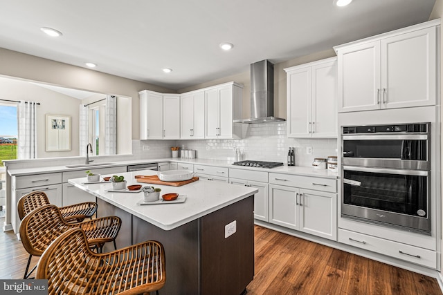 kitchen featuring white cabinetry, stainless steel appliances, a kitchen breakfast bar, a kitchen island, and wall chimney exhaust hood