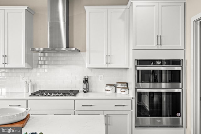 kitchen with stainless steel appliances, decorative backsplash, white cabinets, and wall chimney exhaust hood