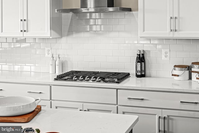 kitchen with tasteful backsplash, wall chimney range hood, stainless steel gas stovetop, light stone countertops, and white cabinets