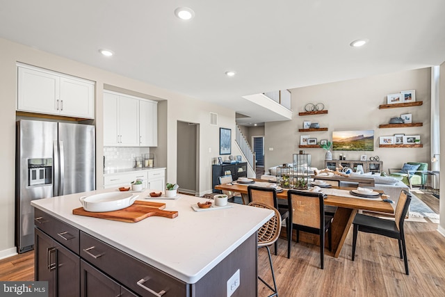 kitchen featuring white cabinets, backsplash, stainless steel fridge, a center island, and light wood-type flooring