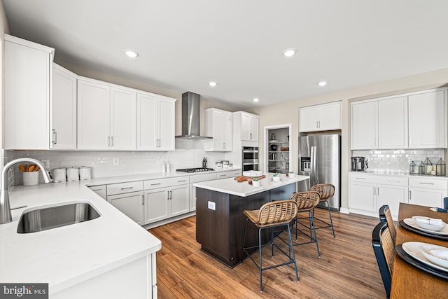 kitchen with appliances with stainless steel finishes, sink, white cabinets, a center island, and wall chimney exhaust hood