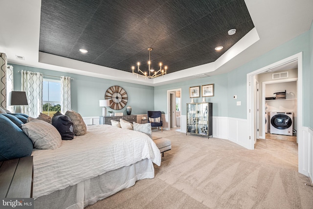 bedroom featuring an inviting chandelier, light colored carpet, a tray ceiling, and washing machine and clothes dryer