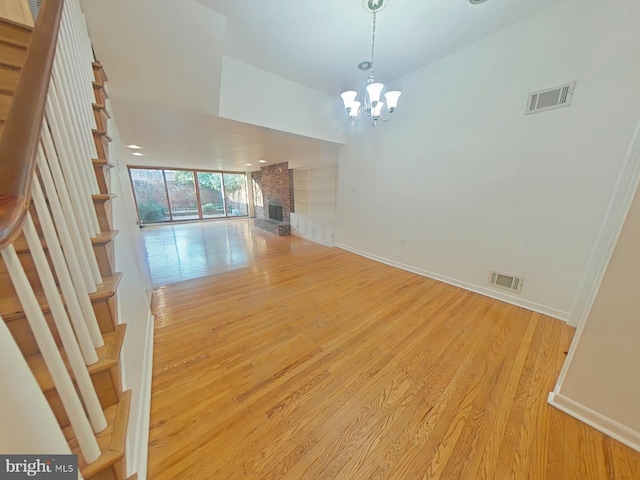 unfurnished living room with a brick fireplace, a notable chandelier, and light wood-type flooring