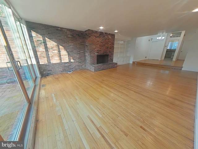 unfurnished living room featuring brick wall, a fireplace, and light hardwood / wood-style floors