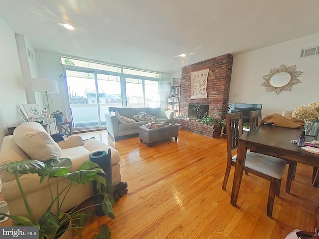 living room featuring a brick fireplace, light hardwood / wood-style floors, and a wall of windows