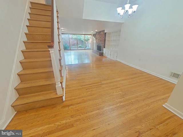 stairway featuring built in features, hardwood / wood-style floors, a fireplace, and an inviting chandelier