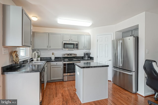 kitchen featuring sink, wood-type flooring, gray cabinets, a kitchen island, and stainless steel appliances