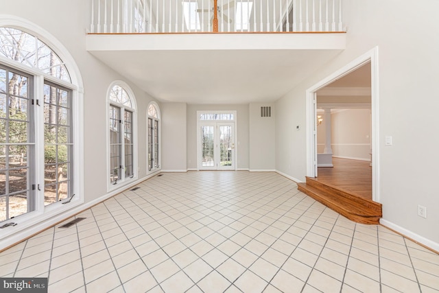 empty room featuring light tile patterned floors, baseboards, a high ceiling, and visible vents