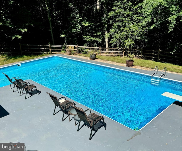 pool with a patio area, fence, and a diving board