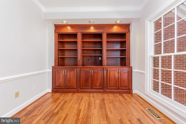 interior space with light wood-style floors, baseboards, visible vents, and crown molding