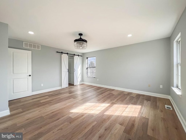 unfurnished bedroom featuring an inviting chandelier, a barn door, and light wood-type flooring