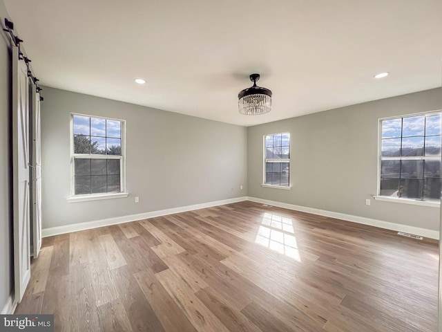 empty room featuring hardwood / wood-style flooring, a barn door, and an inviting chandelier