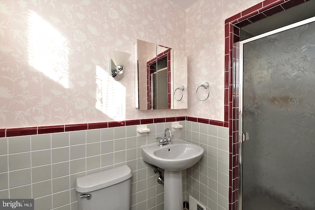 bathroom featuring a shower with door, tile walls, and toilet