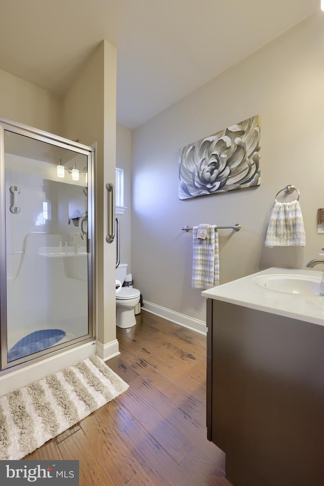 bathroom with wood finished floors, toilet, baseboards, and a stall shower