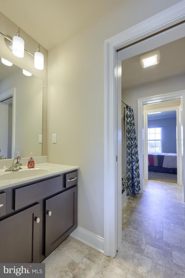 bathroom with baseboards, stone finish floor, vanity, and curtained shower