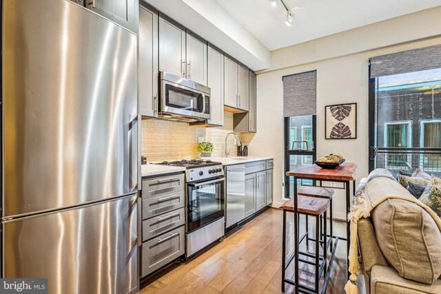 kitchen featuring gray cabinetry, decorative backsplash, stainless steel appliances, and light wood-type flooring