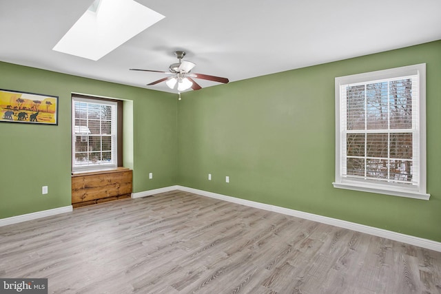 spare room featuring light hardwood / wood-style flooring, ceiling fan, and a skylight