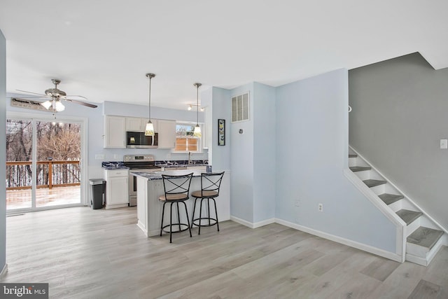 kitchen with a breakfast bar, white cabinets, hanging light fixtures, stainless steel appliances, and light wood-type flooring