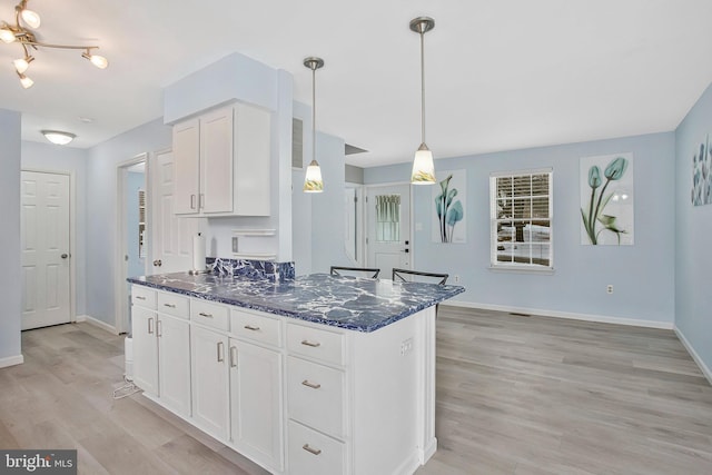 kitchen featuring pendant lighting, dark stone countertops, light hardwood / wood-style flooring, and white cabinets