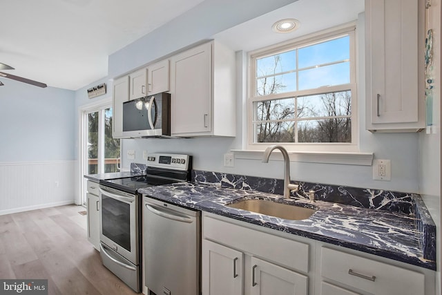 kitchen with sink, white cabinetry, light hardwood / wood-style flooring, appliances with stainless steel finishes, and dark stone counters