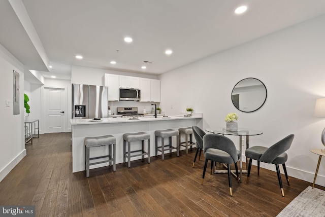 kitchen featuring a breakfast bar, white cabinetry, stainless steel appliances, dark hardwood / wood-style flooring, and kitchen peninsula